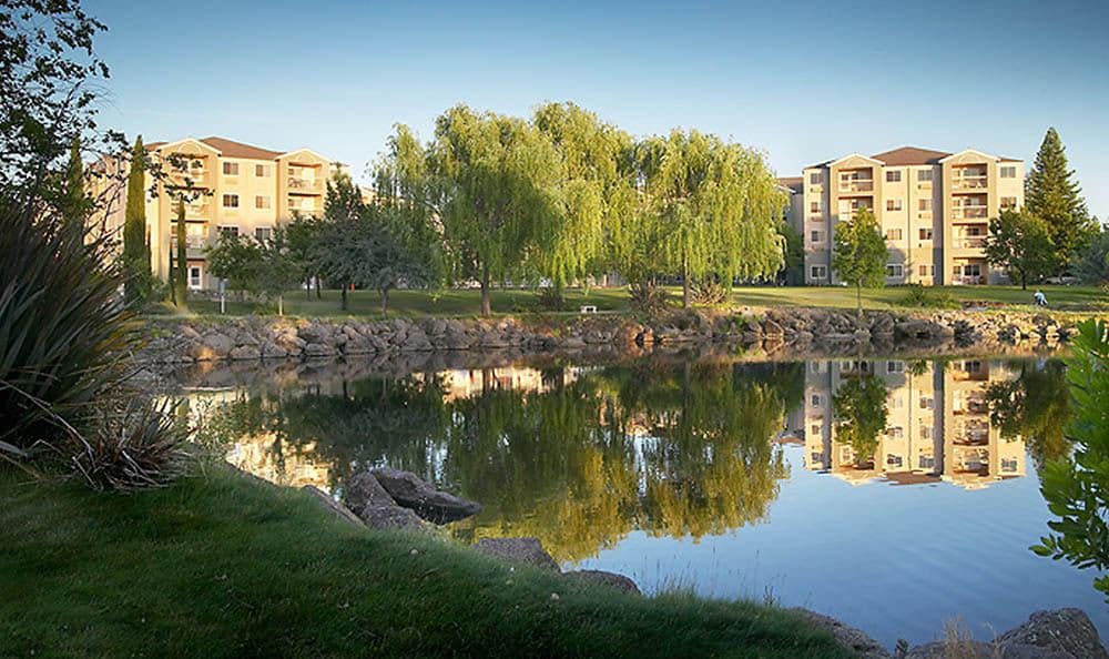 A serene lake reflecting surrounding trees and buildings, set in a peaceful landscape.