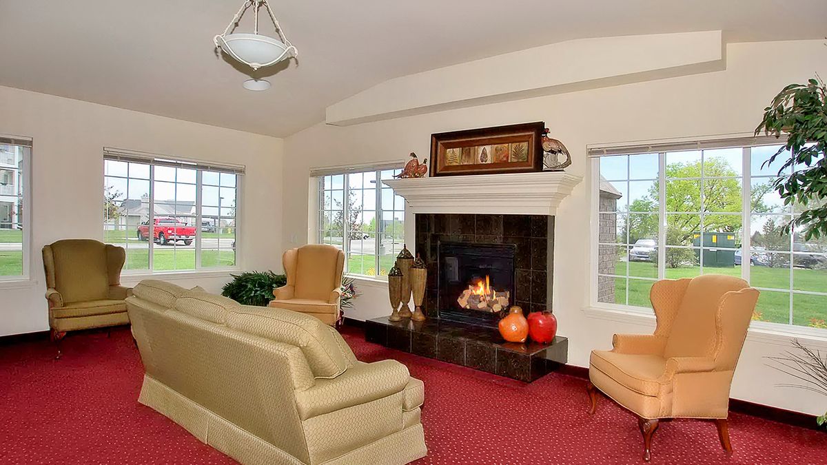 A cozy living room with a lit fireplace, sofa, and bright windows.