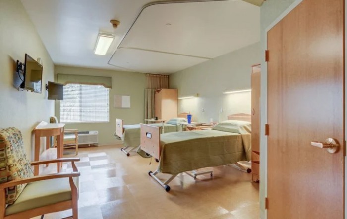A clean and well-organized hospital room with two patient beds and natural light coming through the window.