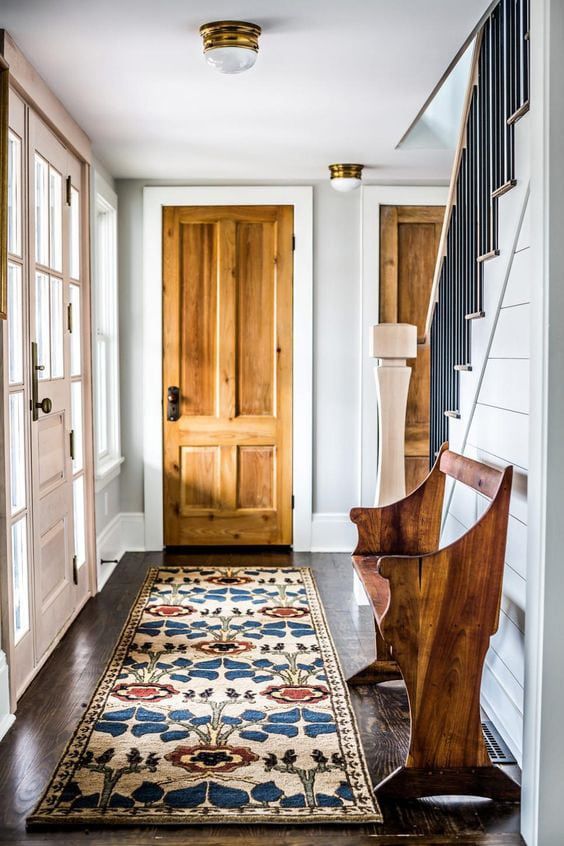 A cozy hallway featuring a wooden door, patterned rug, and a wooden bench alongside a staircase.