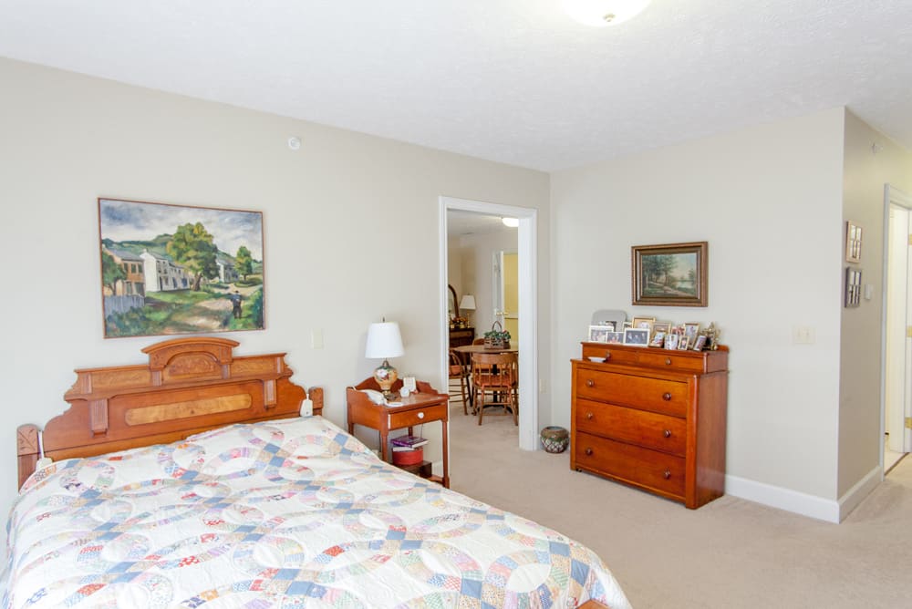 A cozy bedroom with wooden furniture, including a bed and dresser, decorated with paintings and a lamp.