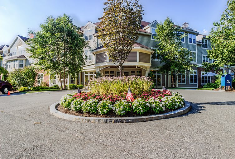 A well-maintained building with a landscaped roundabout featuring flowers and trees.