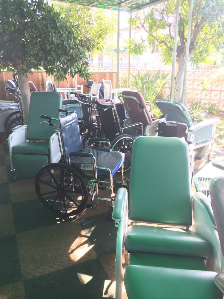 A collection of various wheelchairs and medical chairs arranged outdoors in the sunlight.