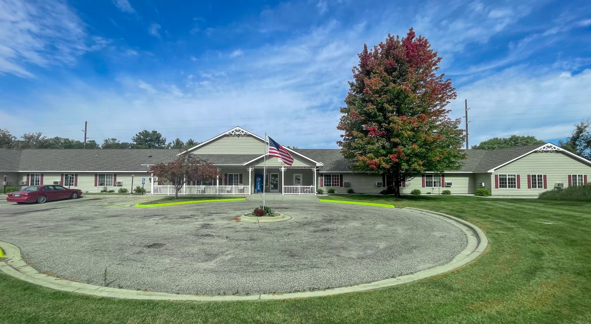A school building with an American flag out front, surrounded by trees showing fall colors and a circular driveway.