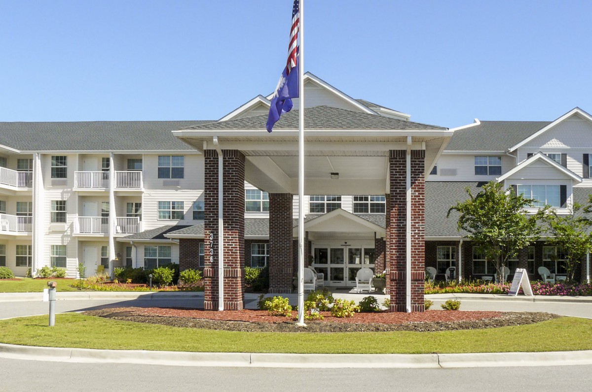 A residential building with a prominent entrance, featuring flags and well-maintained landscaping.