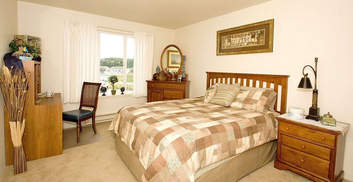 A cozy bedroom with a checkered bedspread, dresser and mirror, and a window offering natural light.