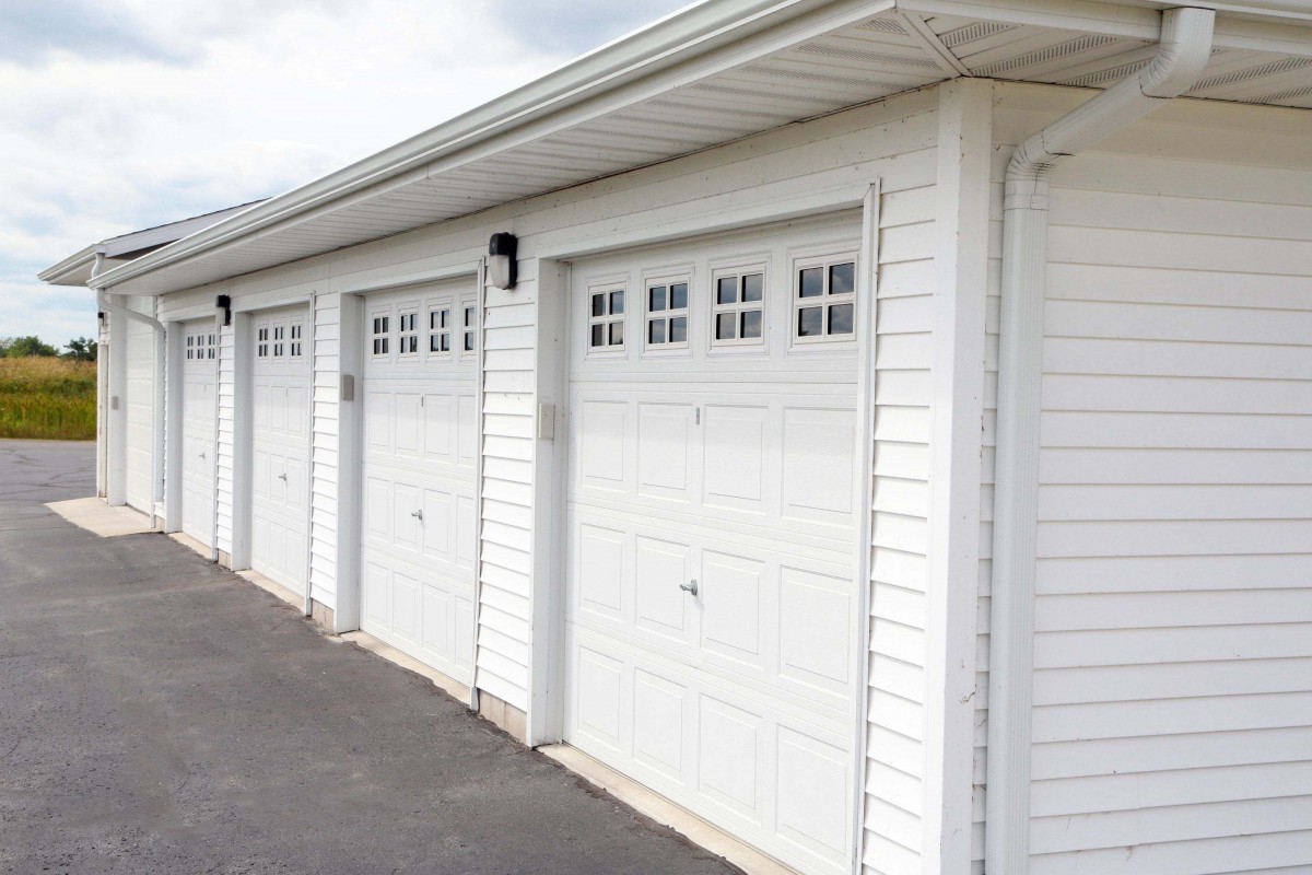 A row of white garage doors along a paved driveway.