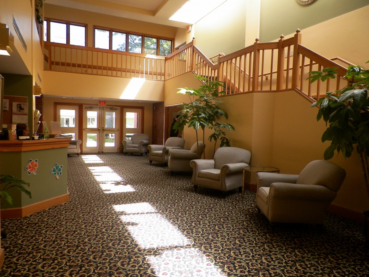 A spacious lobby with armchairs, stairs, and natural sunlight streaming in.