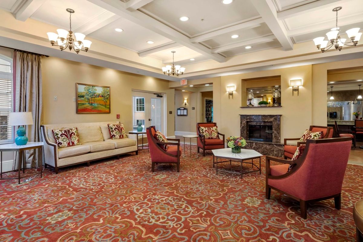 A well-appointed living room featuring a cozy seating area with armchairs and a sofa, complemented by elegant chandeliers and a warm-toned carpet.