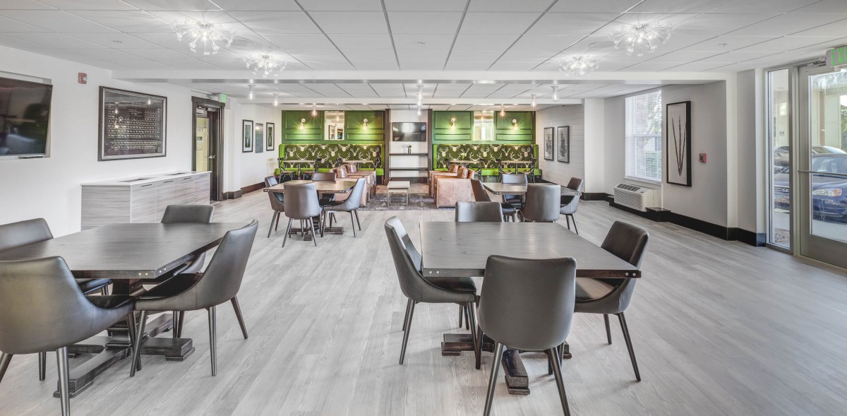 A modern office workspace featuring an open seating area with a green wall and contemporary furniture.