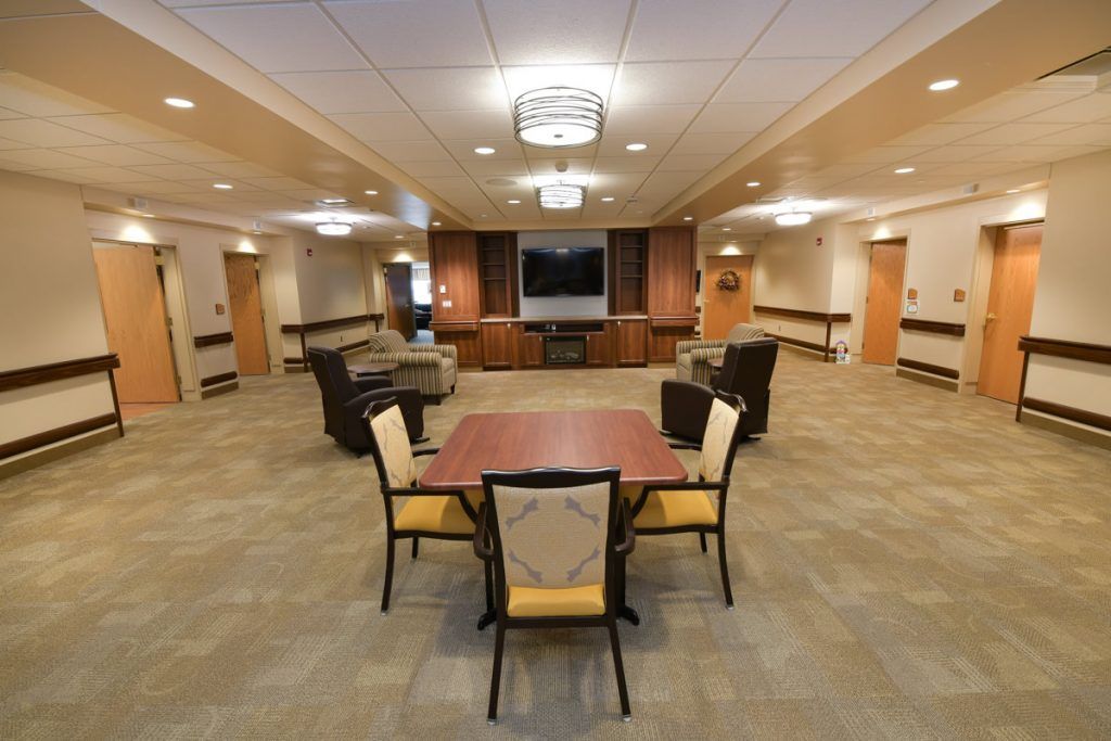 A spacious and well-lit lounge area featuring a central table surrounded by chairs, with a television and seating in the background.