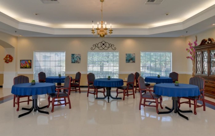 A well-lit dining room with blue tablecloths covering round tables and chairs arranged around them.