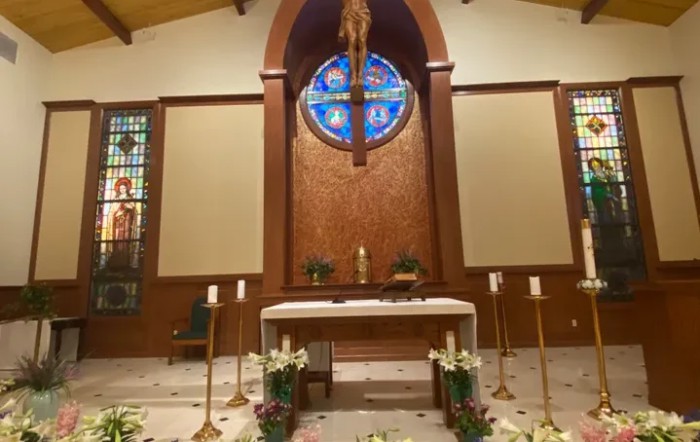 Interior of a church with an altar, crucifix, and stained glass window.