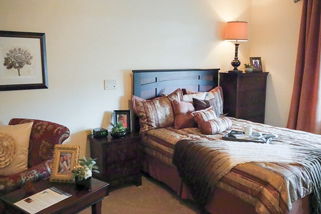 A cozy bedroom with a neatly made bed, bedside table, and warm lighting.