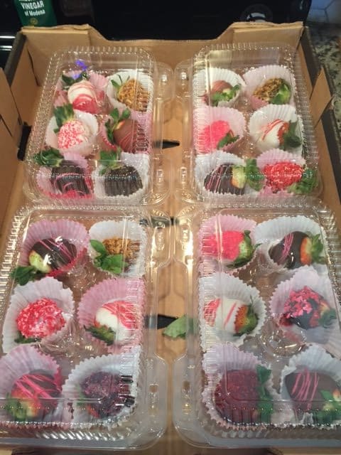 A selection of beautifully decorated chocolate-covered strawberries in clear packaging.