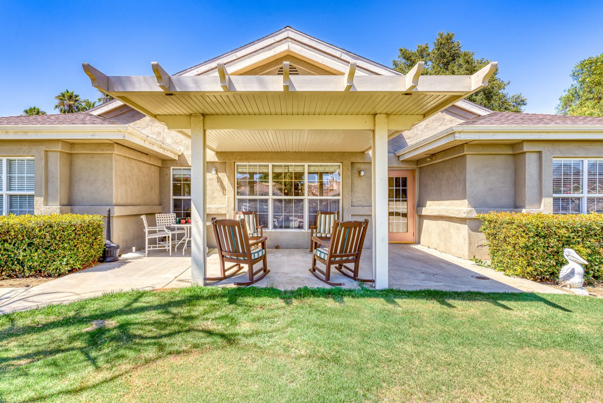 A cozy outdoor patio with a pergola and rocking chairs, overlooking a green lawn.