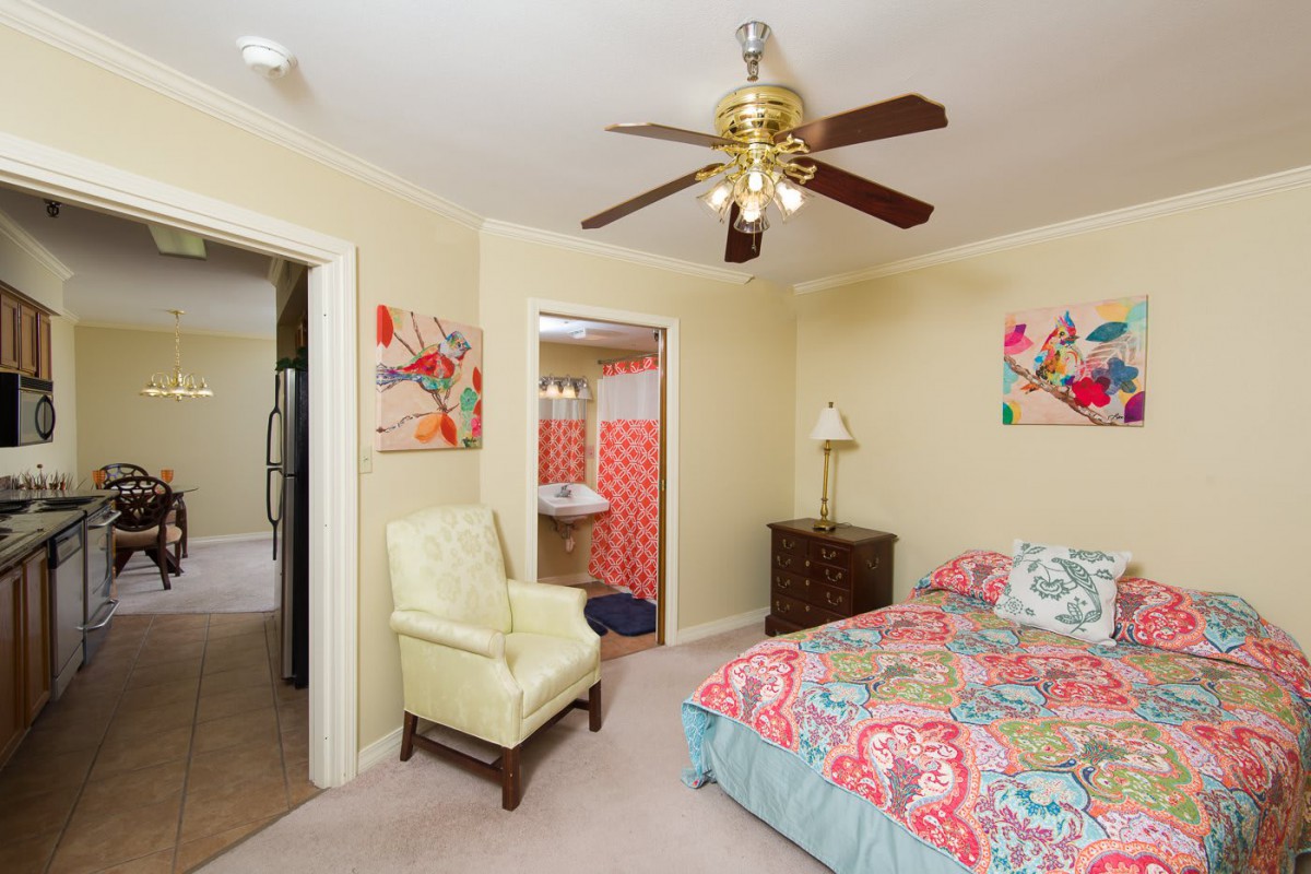 A cozy bedroom featuring a ceiling fan, colorful bedding, an armchair, and vibrant wall art.