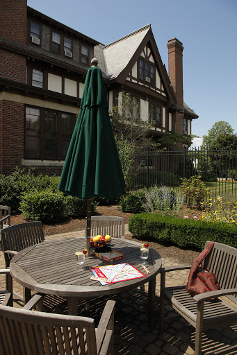 A cozy outdoor dining setup featuring a wooden table under a green umbrella, surrounded by lush gardens.