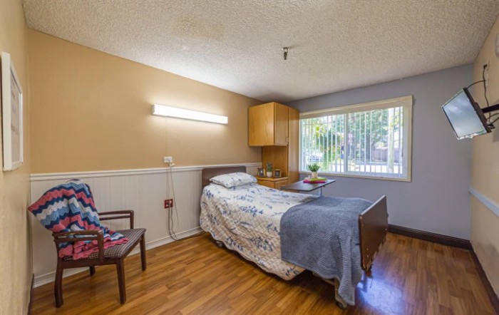 A well-lit bedroom with a single bed, wooden floors, and a window providing natural light.