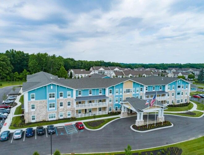 Aerial view of a blue and beige apartment complex with a parking lot and surrounding greenery.