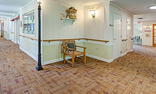 A cozy hallway with wooden flooring, featuring a chair, wall art, sconce lighting, and a floor lamp.