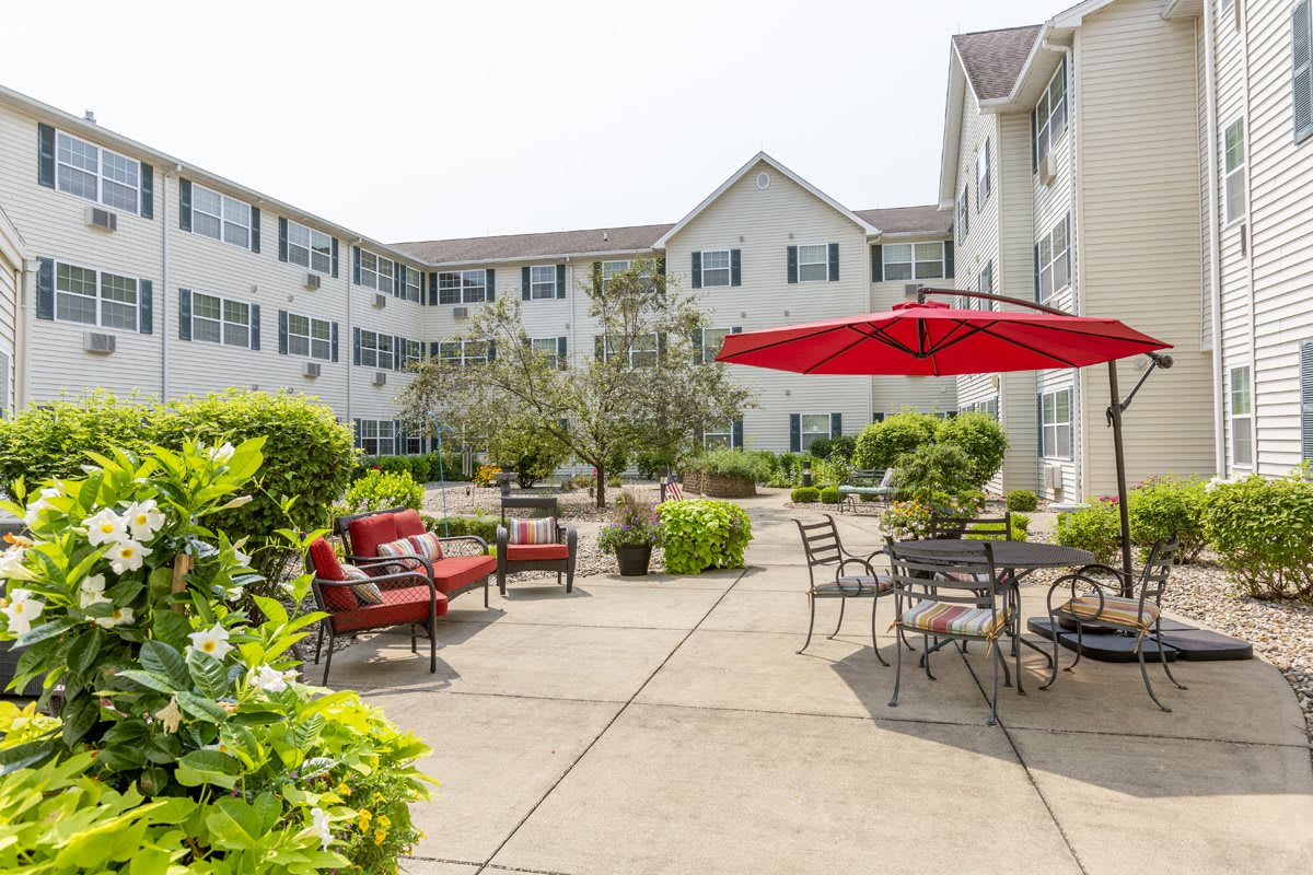 A spacious courtyard with seating areas and a large red umbrella, surrounded by a multi-story apartment building.