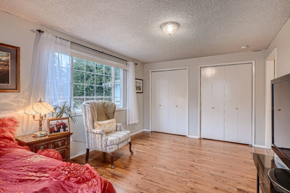 A cozy bedroom with hardwood floors, featuring an armchair by the window and two closets.