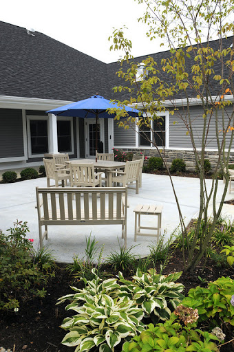 A serene outdoor patio setup featuring wooden furniture, an umbrella for shade, and lush greenery.