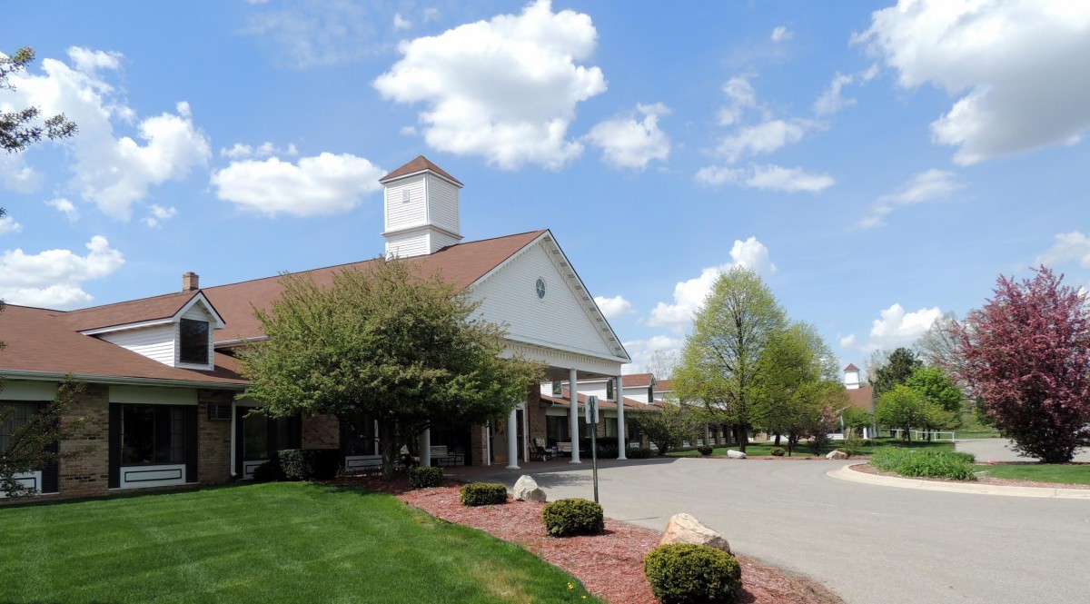 A picturesque building with a tower under a blue sky, surrounded by trees and landscaped grounds.