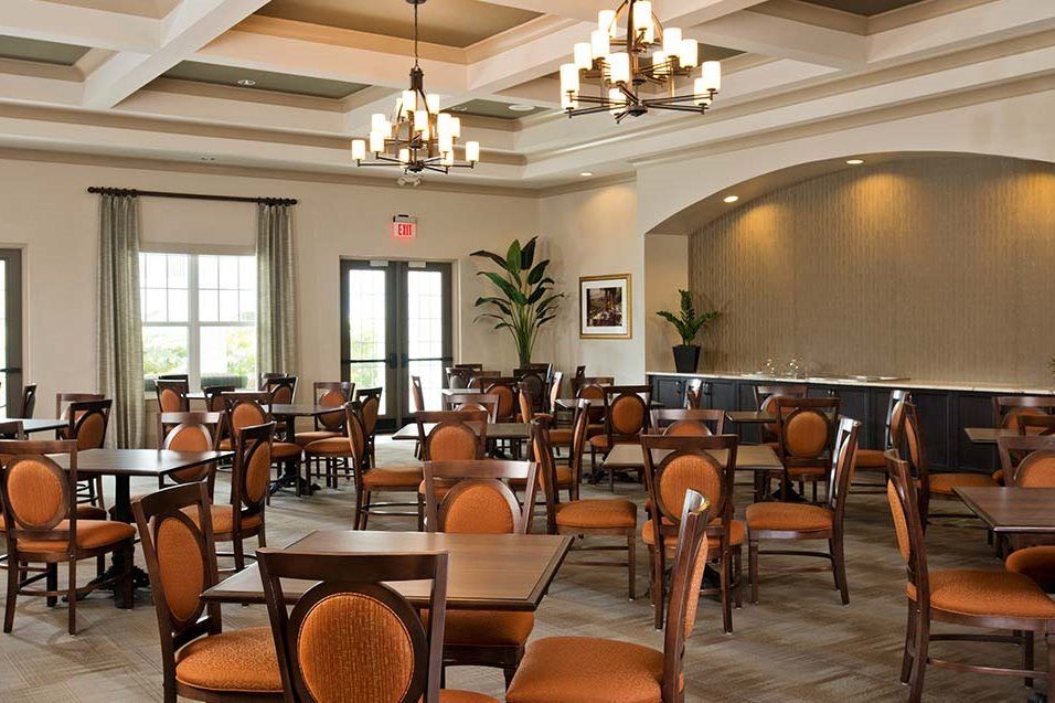 An elegantly furnished dining room with wooden tables and orange-cushioned chairs under chandeliers.