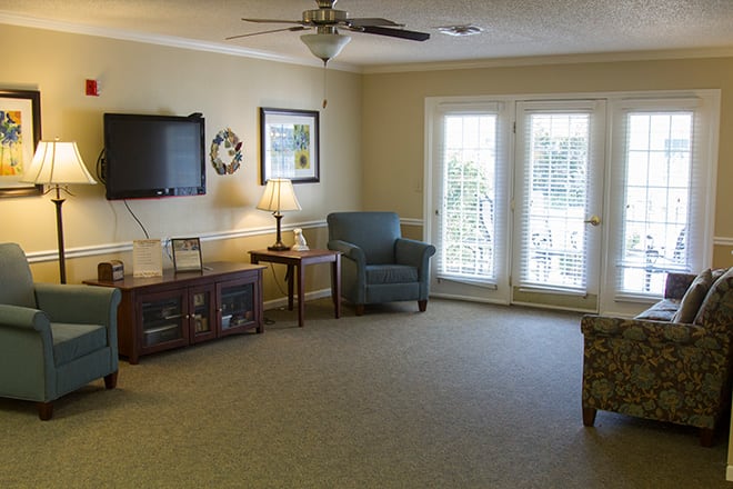 A cozy living room with a TV, armchair, and lamps.