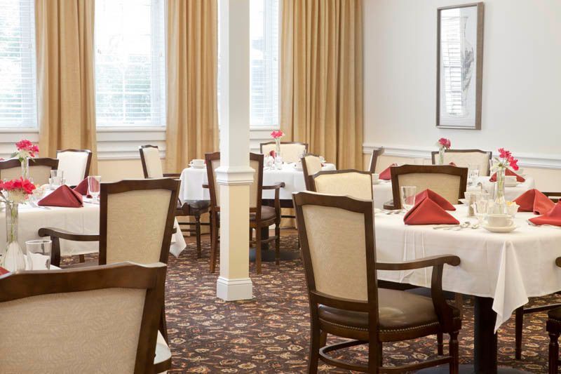 A neatly arranged dining room with tables set with white tablecloths and red napkins.