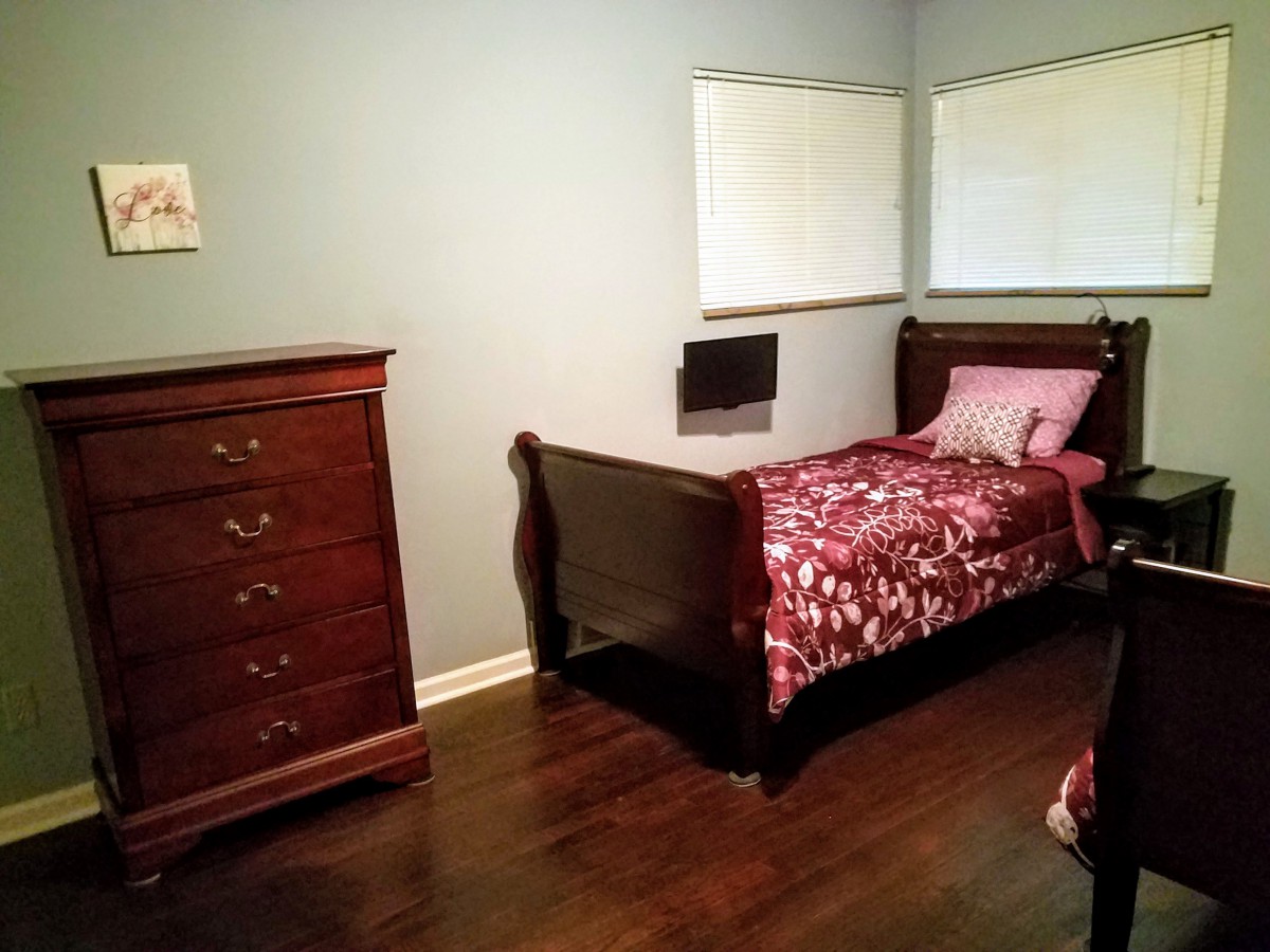 A cozy bedroom with a wooden bed and dresser, featuring dark wood flooring.