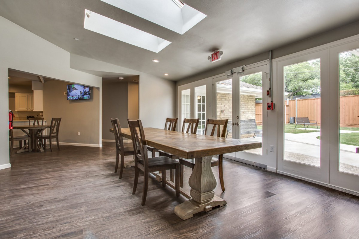 A modern dining room with a long wooden table, surrounded by chairs, featuring skylights and glass doors leading outside.
