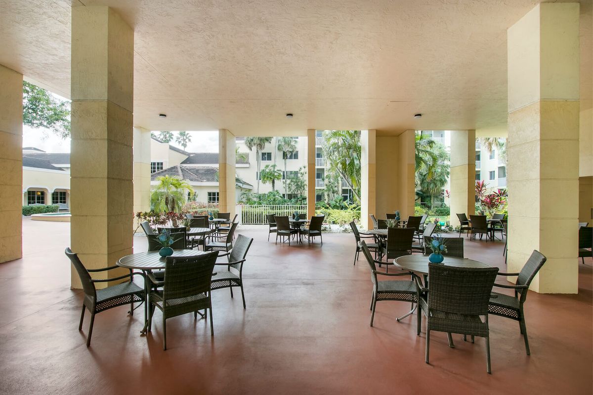 A covered patio area with tables and chairs overlooking a garden and residential buildings.