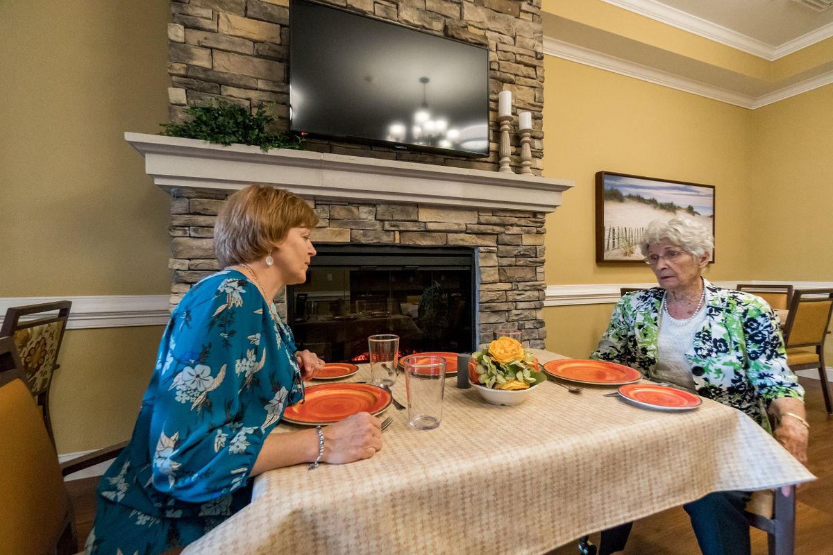 Two people sitting at a dining table having a conversation in a cozy room with a fireplace and television.