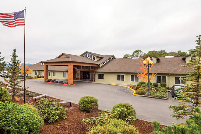 A hotel building with a well-maintained garden and a parking area at the front.