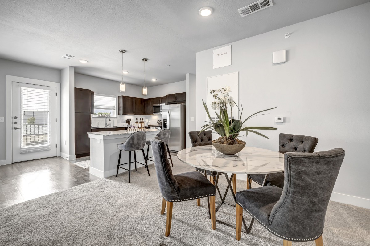 A modern open-concept kitchen and dining area featuring a marble dining table, bar stools at the island counter, and stainless steel appliances.