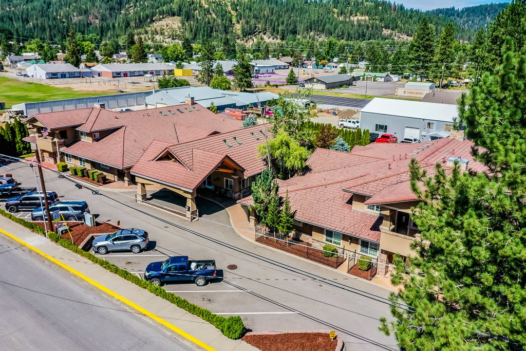 Aerial view of a suburban area with buildings, cars parked along the road, and trees surrounding the landscape.