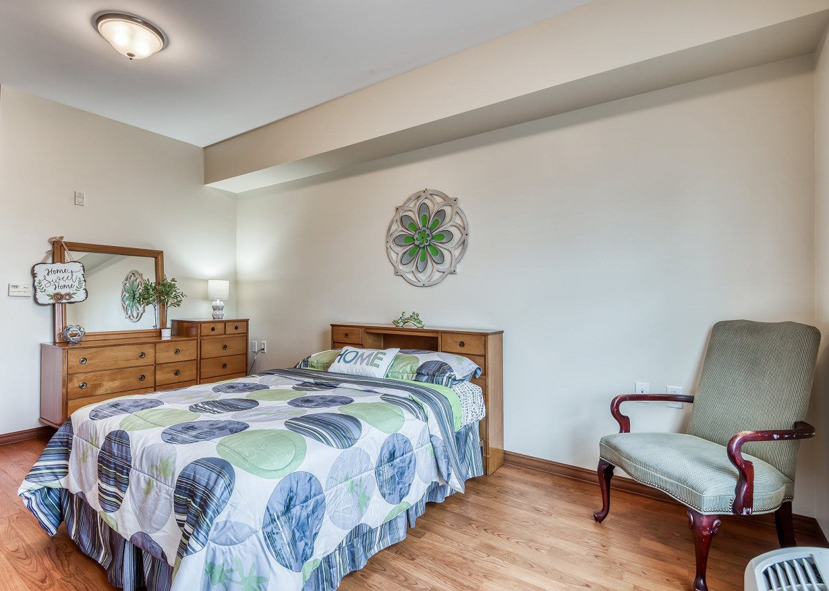 A cozy bedroom featuring a bed with a patterned quilt, wooden furniture, and a decorative wall piece.