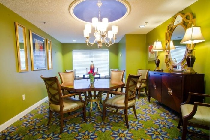 A vibrantly decorated dining room featuring a wooden table with chairs, a chandelier, and colorful patterned carpet.