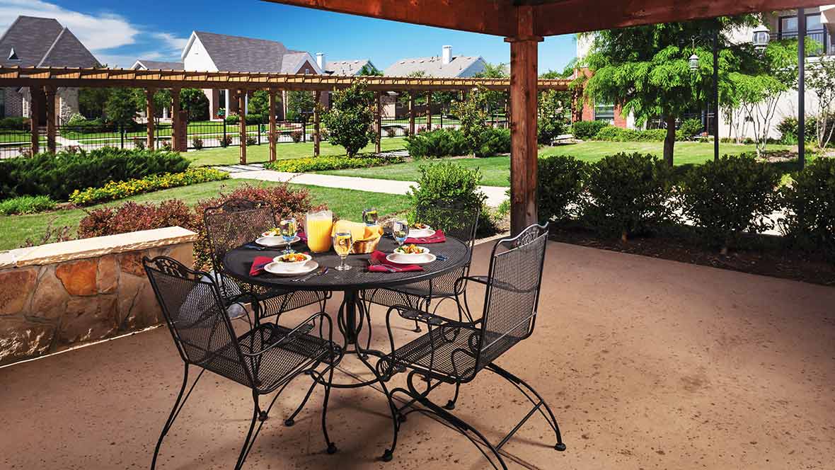 A cozy outdoor patio with a table set for breakfast, overlooking a well-maintained garden.