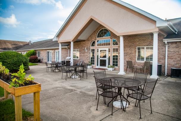A patio area with metal tables and chairs in front of a brick building with arched windows.