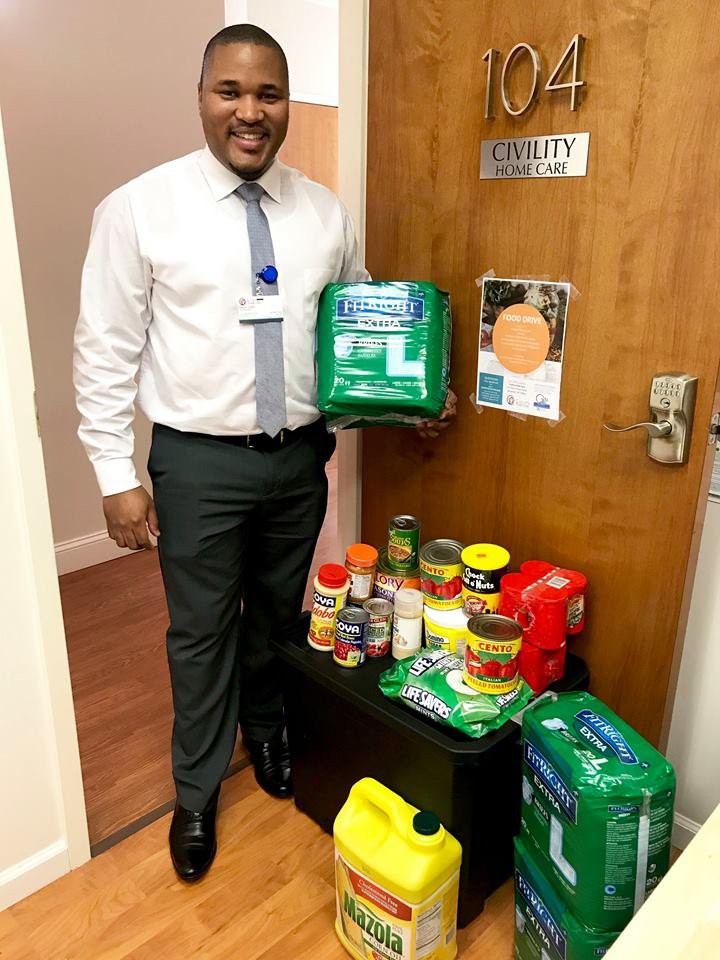 A person standing by a door with various donated food supplies and essentials.