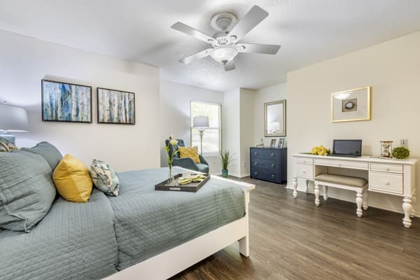 A modern bedroom with stylish decor, featuring a comfortable bed, ceiling fan, and a workspace.