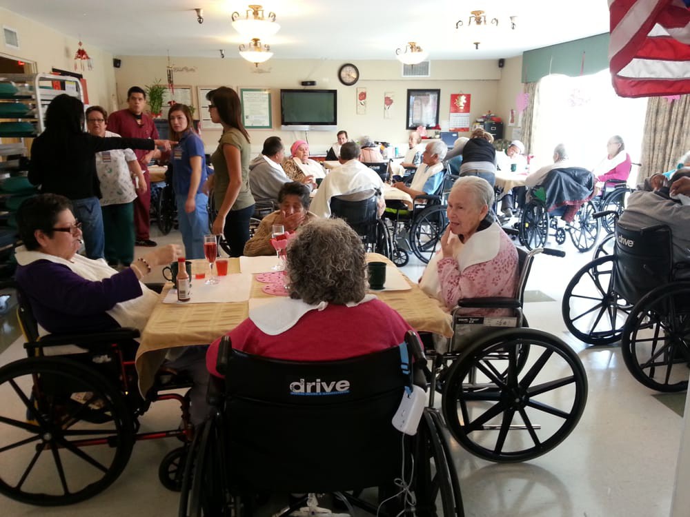 Elderly individuals in wheelchairs gathered in a communal room at a nursing home.