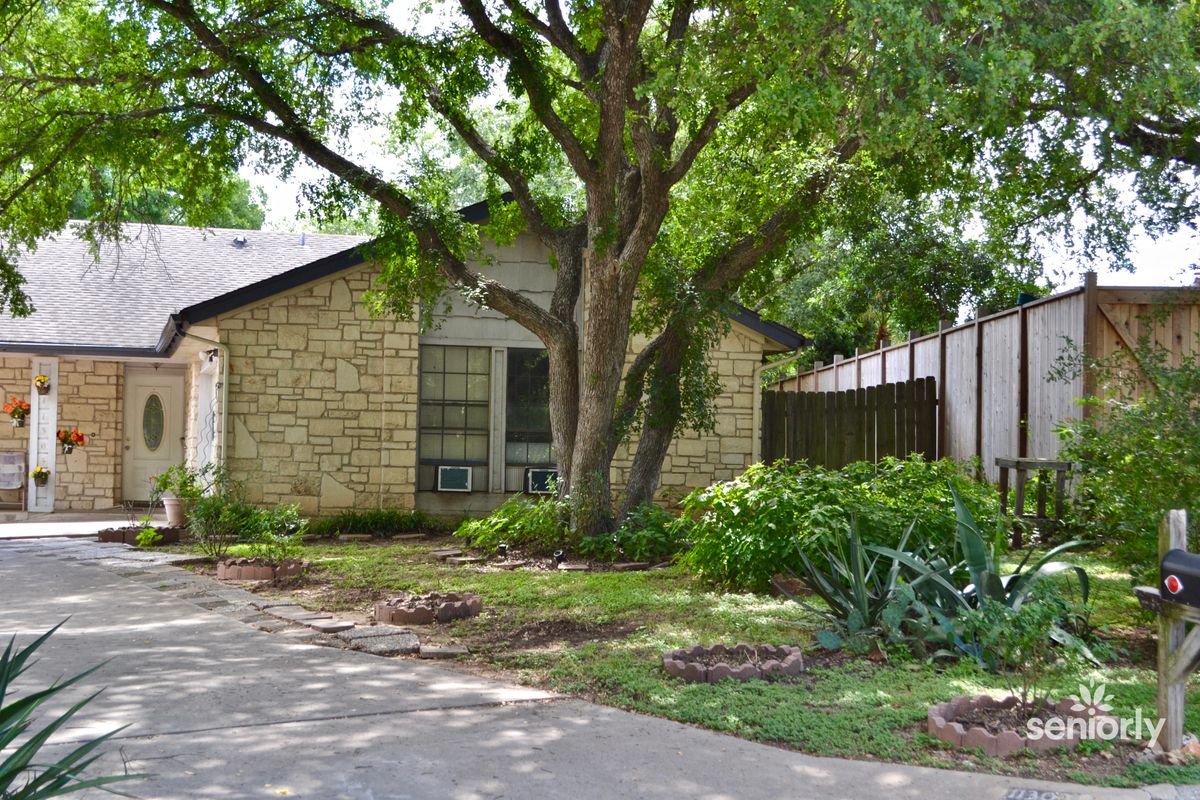 A cozy residential house with a stone exterior, surrounded by lush greenery and a spacious driveway.