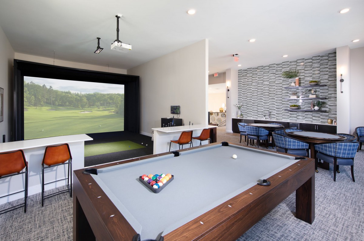 A modern game room featuring a billiards table and a golf simulator, designed for home entertainment.