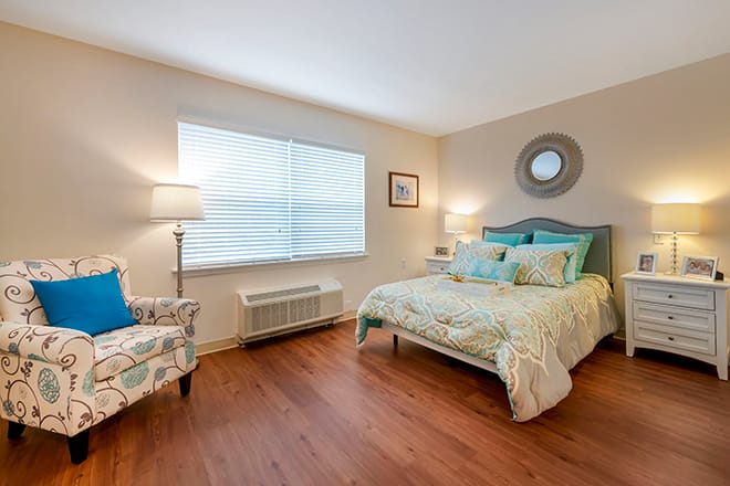 A cozy bedroom with a neatly made bed, soft lighting, and wooden flooring.