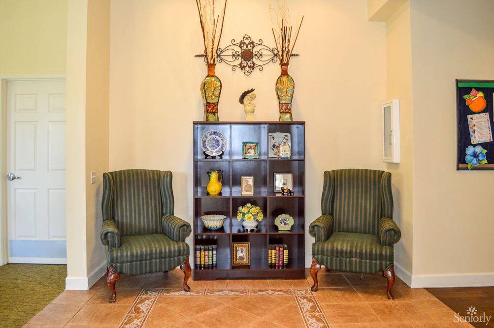A cozy living room corner featuring two green striped chairs flanking a decorative bookshelf with various ornaments.
